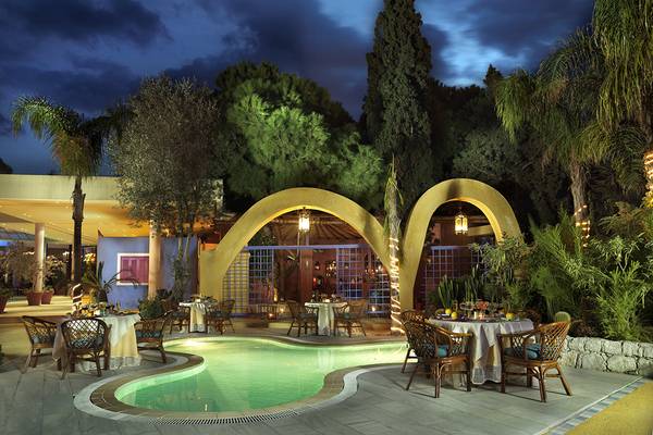 Außenbereich des Dionysos Hotels bei Nacht mit beleuchtetem Swimmingpool und runden Arkaden.