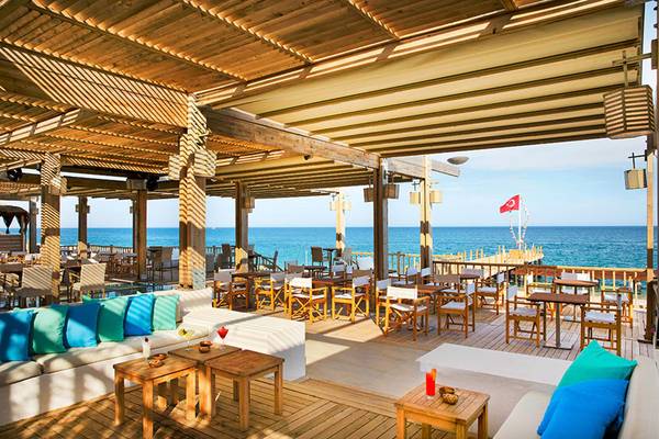 Außenterrasse des Marti Myra Hotels mit Blick auf das Meer, gesäumt von Holztischen und Stühlen, blauen Kissen und einem türkischen Flaggen.