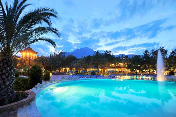 Der Außenpool des Marti Myra Hotels bei Nacht, mit Palmen, Lounge-Stühlen und einer Fontäne.