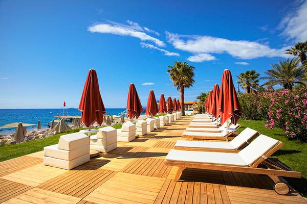 Reihe von weißen Lounge-Stühlen mit roten Sonnenschirmen auf einer Holzterrasse am Strand