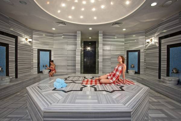Zwei Frauen im Titan Select Hotel in der Sauna, eine sitzt auf einem roten Teppich.