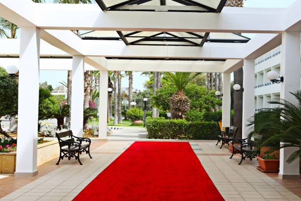 Eingang des Dome Beach Hotel & Resort mit einem roten Teppich, umgeben von Gärten und Bäumen.