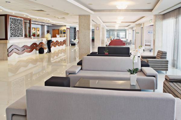Innenansicht der Lobby des Dome Beach Hotel & Resort mit Rezeptionstresen, Sofas und einem Mitarbeiter