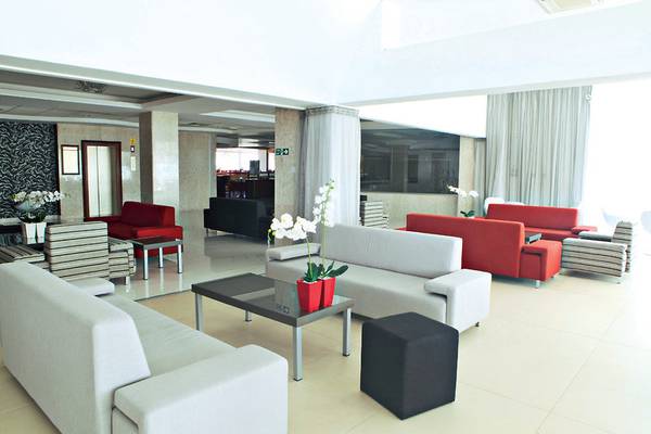 Lobby des Dome Beach Hotel & Resort mit weißen Sofas, Tischen und roten Sesseln.