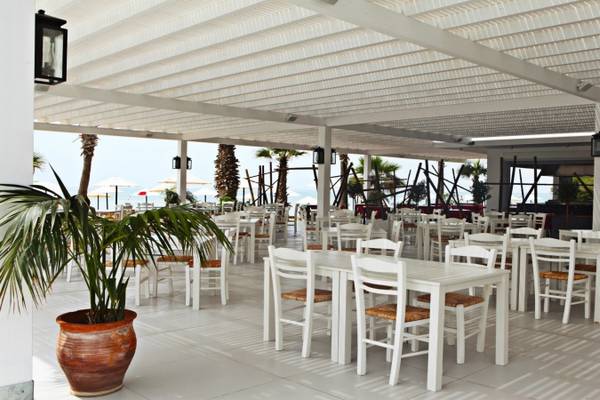 Außenterrasse des Dome Beach Hotel & Resort mit weißen Tischen und Stühlen und einer Palme im Topf.