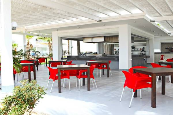 Foto der Außenterrasse des Dome Beach Hotel & Resort mit roten Stühlen und Tischen unter einem Pergoladach.