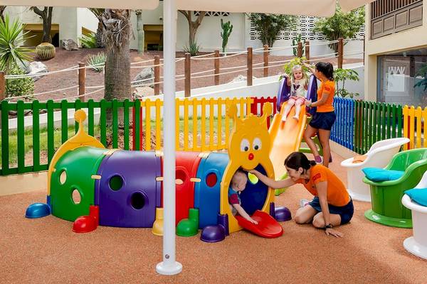 Kinderspielplatz im Freien im H10 Rubicon Palace Hotel mit bunten Spielgeräten und einer Frau, die ein Kind beobachtet.