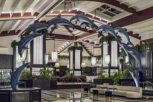 Ein Bild von der Lobby des H10 Rubicon Palace Hotels mit Delfin-Skulpturen, Pflanzen und Möbeln.