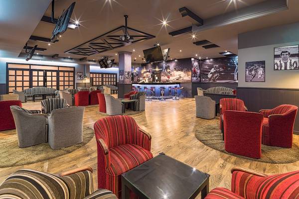 Loungebereich des H10 Rubicon Palace Hotels mit roten und grauen Stühlen, Holzboden und Fernsehern.