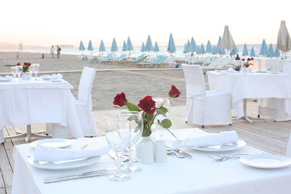 Ein Tisch auf der Strandpromenade des Minos Mare Royal Hotels, dekoriert mit roten Rosen und weißen Tischdecken.