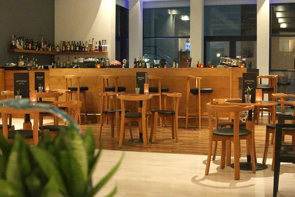 Innenansicht der Bar im Minos Mare Royal Hotel mit Holztischen und Stühlen.