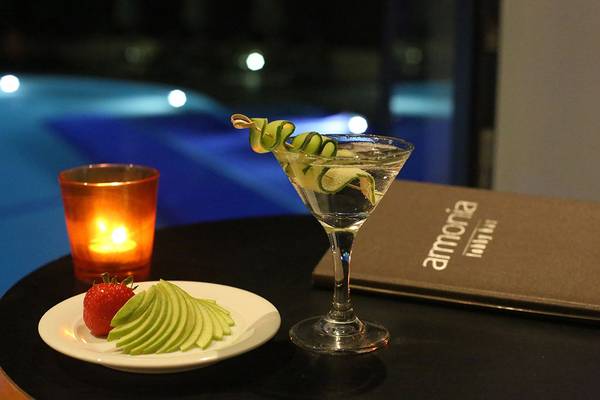 Cocktailglas mit Apfelscheiben und Erdbeere auf einer Platte neben einem Teelicht und einem Buch im Minos Mare Royal Hotel.