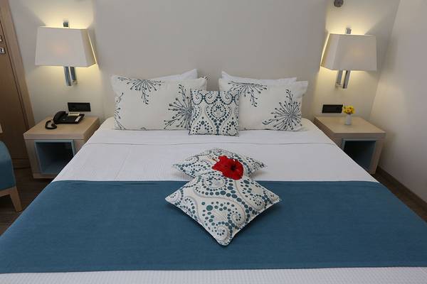 Ein gepflegtes Bett im Minos Mare Royal Hotel mit blauen und weißen Kissen und einer roten Blume.