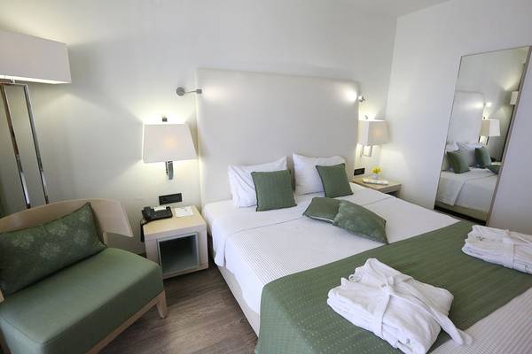 Hotelzimmer im Minos Mare Royal mit grünen Kissen und einem weißen Bett.