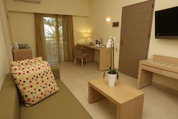Wohnzimmer des Minos Mare Royal Hotels mit grünem Sofa, Tisch, Deko-Pflanze und Fernseher.