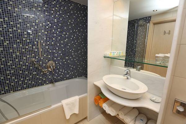 Badezimmer im Minos Mare Royal Hotel mit Badewanne, Waschbecken und blauen Fliesen.
