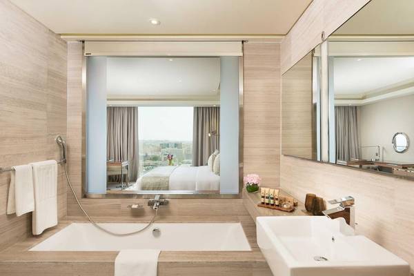 Badezimmer im Grand Millennium Muscat mit Badewanne, Spiegeln und Blick auf das Bett