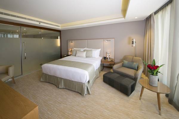 Hotelzimmer im Grand Millennium Muscat mit Doppelbett, Sesseln und Tisch mit Blumen.