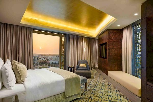 Innenansicht einer Suite im Grand Millennium Muscat Hotel mit Bett, Fenster und Stadtblick