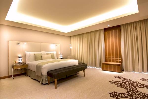 Schlafzimmer im Grand Millennium Muscat Hotel mit Doppelbett, Nachttischen und Wandleuchten.