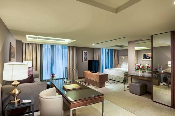 Innenansicht der Suite im Grand Millennium Muscat mit Wohnzimmer, Schreibtisch und Bettbereich.