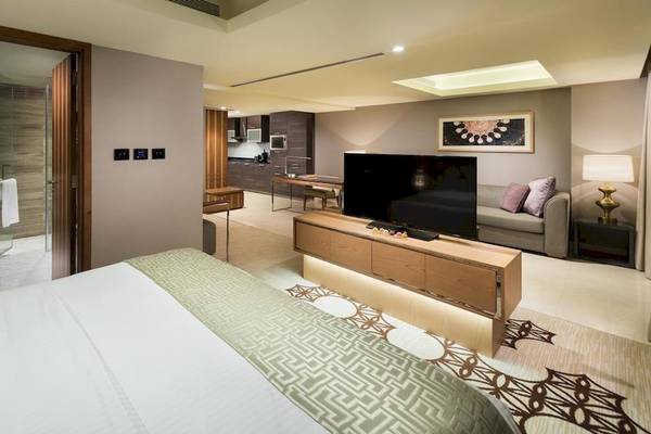 Innenansicht einer Suite im Grand Millennium Muscat mit Bett, Fernseher, Sofa und Dusche
