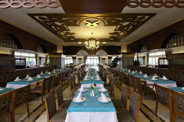 Restaurant im Adalya Bliss Hotel mit gedeckten Tischen und einer langen Tafel in der Mitte.