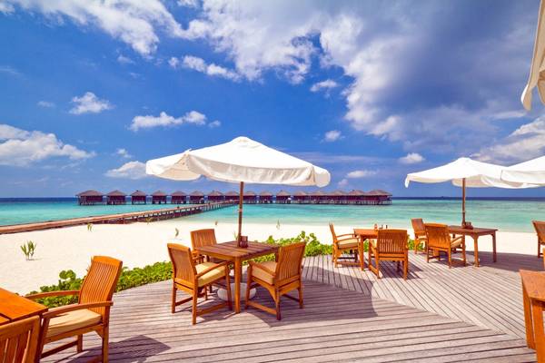 Terrasse des Filitheyo Island Resorts mit Tischen und Umbrellas vor einem blauen Himmel und Meer
