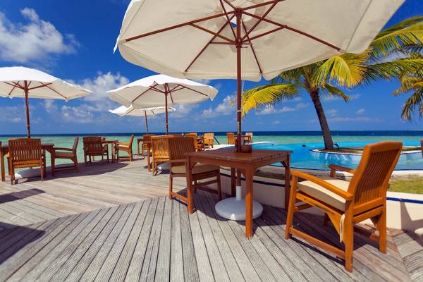 Terrasse des Filitheyo Island Resorts mit Holztischen, Stühlen und Sonnenschirmen am Meer