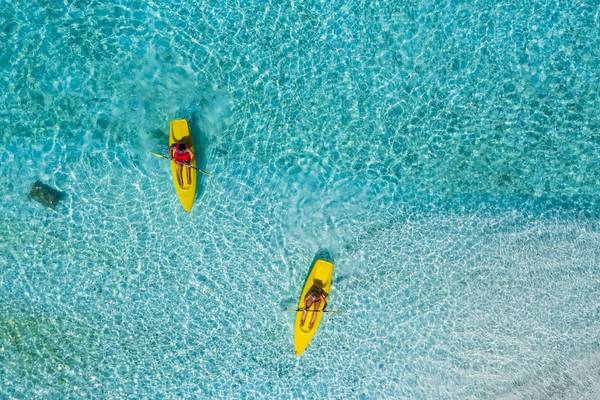 Zwei Personen in gelben Kajaks rudern im kristallklaren Wasser neben dem Filitheyo Island Resort.