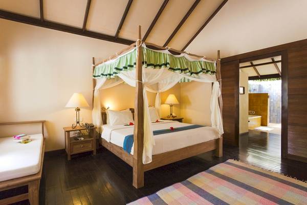 Doppelbett im Zimmer des Filitheyo Island Resorts mit grüner Vorhang und Blumen auf dem Bett.