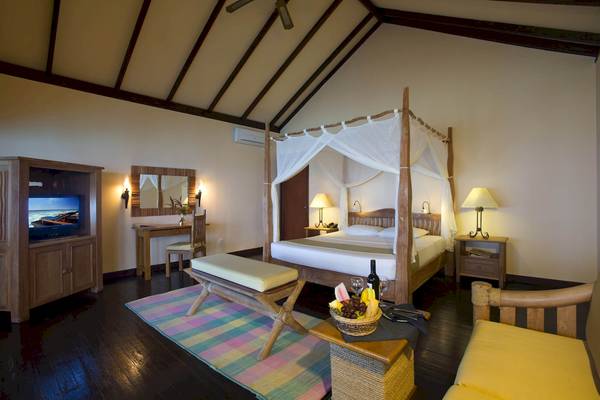 Innenansicht einer Suite im Filitheyo Island Resort mit Bett, Fernseher und Obstkorb.
