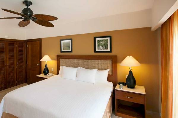 Hotelzimmer im Occidental Caribe mit Doppelbett, Nachttischen, Deckenventilator und Wandbildern.