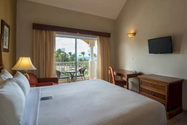 Hotelzimmer im Occidental Caribe mit großem Bett, Schreibtisch, Fernseher und Balkon mit Meerblick.