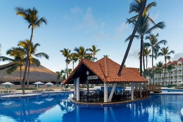 Pool mit Hütte im Occidental Caribe Hotel, umgeben von Palmen und Sonnenliegen.