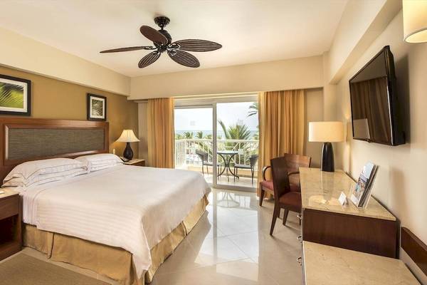 Hotelzimmer im Occidental Caribe mit Bett, Schreibtisch und Meerblick durch Glastür.