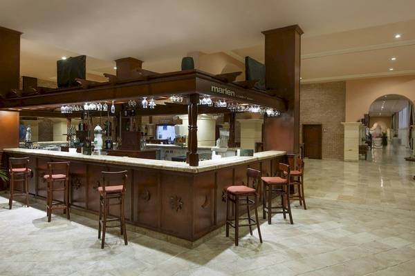 Die Lobby-Bar des Occidental Caribe Hotels mit Holzbar, Stühlen und Fernseher.