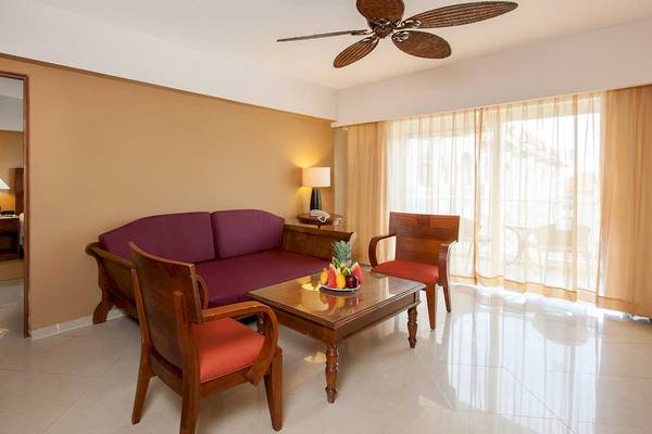 Hotelzimmer des Occidental Caribe mit Möbeln, Tisch, Obstteller, Fenstern und Deckenventilator.