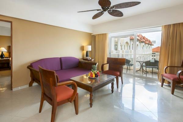 Hotelzimmer im Occidental Caribe mit violettem Sofa, Tisch und Balkonzugang.