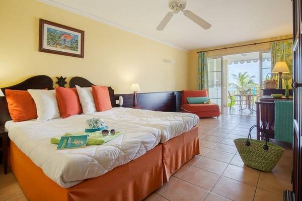 Doppelzimmer im Pierre & Vacances Village Club Sainte-Anne mit zwei Betten, Kissen und Decken, farbenfrohem Dekor und Zugang zu einem Balkon.