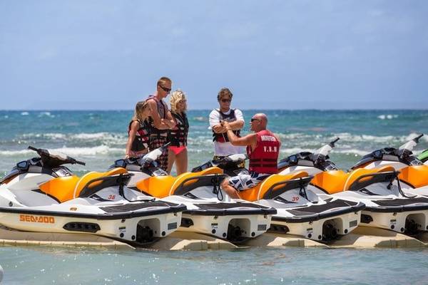 Personen stehen am Strand neben mehreren Jet-Skis auf dem Wasser.