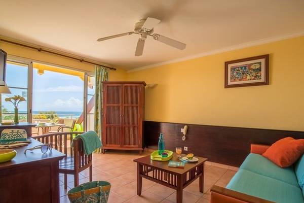 Hotelzimmer mit Balkon und Meerblick, gelbe Wände, Couch, Tisch und Aussicht auf das Meer.