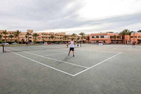 Tennisplatz im Beach Albatros Resort mit einem Spieler und Gebäude im Hintergrund.