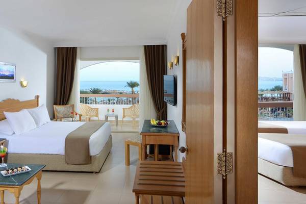 Hotelzimmer mit Meerblick, Bett, Couch, Tisch, Fernseher und Balkon.