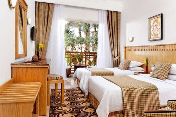 Innenansicht eines Doppelzimmers im Beach Albatros Resort mit zwei Betten, einem Balkon und Blick auf Palmen.