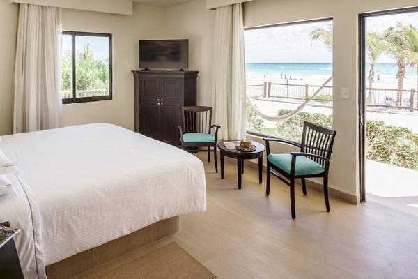 Innenansicht eines Hotelzimmers im Allegro Playacar mit Blick auf das Meer, inklusive Bett, Fernseher, Tisch und Stühlen.