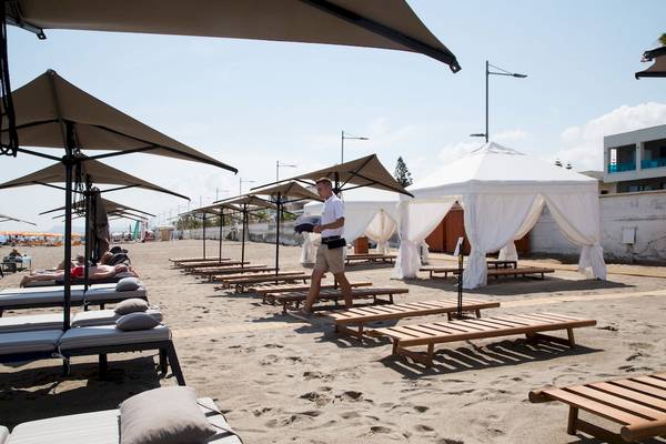 Mann geht an Sonnenliegen am Strand des Ikones Seafront Luxury Suites Hotels vorbei