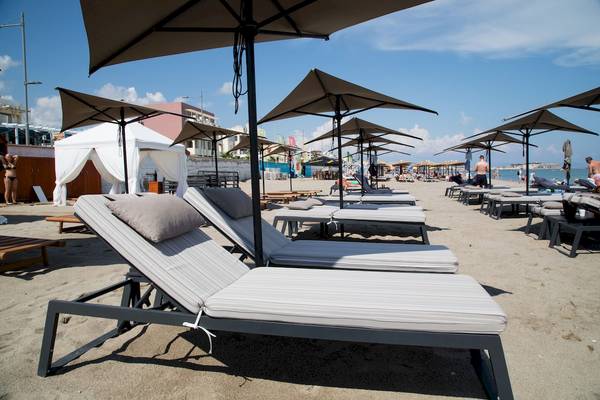 Strand mit Sonnenliegen und Sonnenschirmen im Ikones Seafront Luxury Suites Hotel