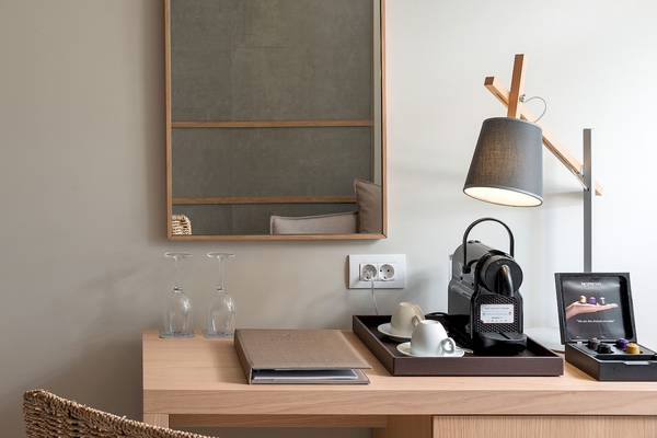 Schreibtisch im Zimmer der Ikones Seafront Luxury Suites mit Lampe, Kaffeemaschine, Gläsern und Notizbuch.