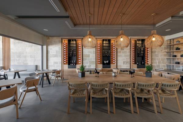 Innenansicht des Restaurants im Ikones Seafront Luxury Suites Hotel mit Holztischen und Stühlen, Holzlampen und Weinregalen.